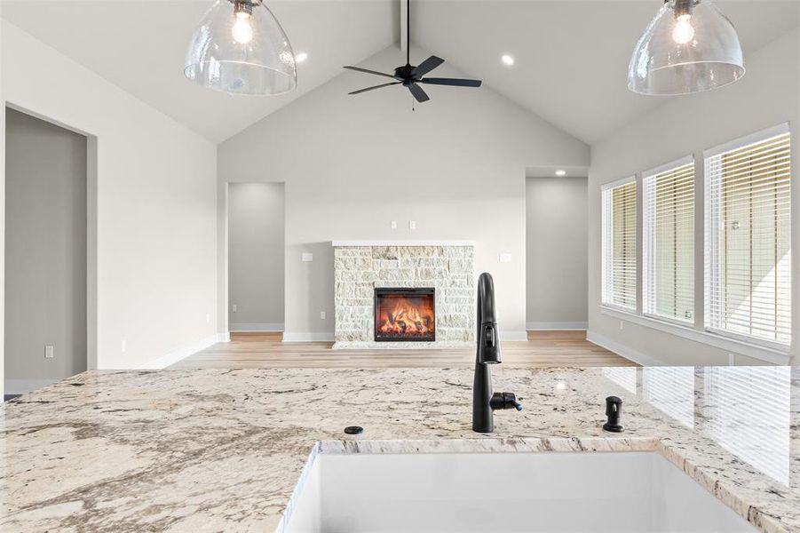Unfurnished living room with a stone fireplace, beam ceiling, high vaulted ceiling, ceiling fan, and light wood-style flooring