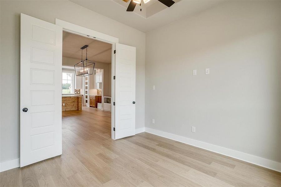 Empty room featuring ceiling fan with notable chandelier and light hardwood / wood-style flooring