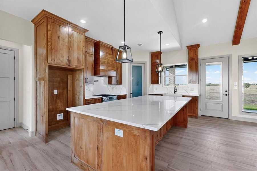 Kitchen with brown cabinets, a kitchen island, light wood-style floors, pendant lighting, and light stone counters Kitchen with brown cabinets, a kitchen island, light wood-style floors, pendant lighting, and light stone counters