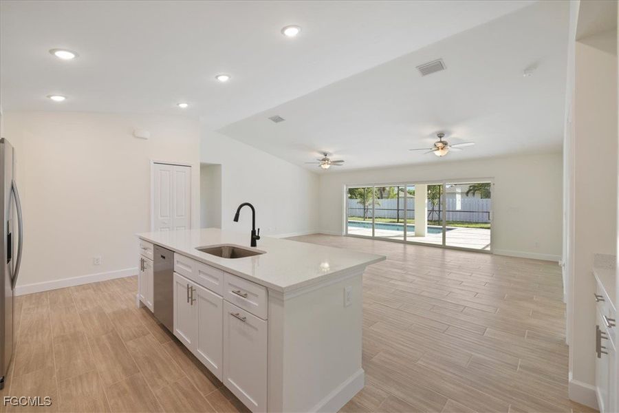 Kitchen with white cabinetry, wood finish floors, a center island with sink, lofted ceiling, and open floor plan