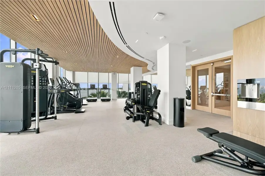 Fitness center featuring floor-to-ceiling windows, slatted wood-finish ceiling, recessed lighting, and wall-mounted water dispenser Fitness center featuring floor-to-ceiling windows, slatted wood-finish ceiling, recessed lighting, and wall-mounted water dispenser