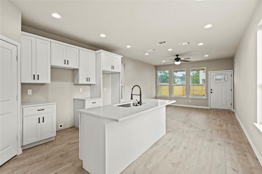 Kitchen featuring light hardwood / wood-style flooring, white cabinetry, sink, ceiling fan, and a center island with sink