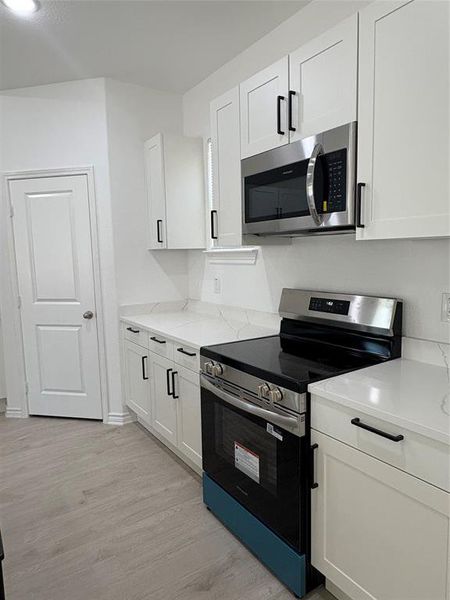 Kitchen with appliances with stainless steel finishes, white cabinetry, light wood-style floors, and light stone counters