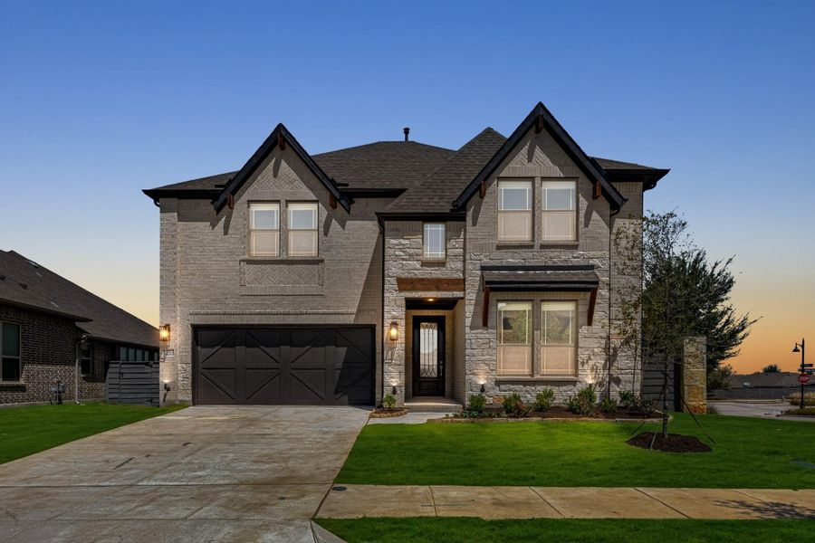 Two-story home with stone and brick exterior, two-car garage, and manicured front lawn at dusk