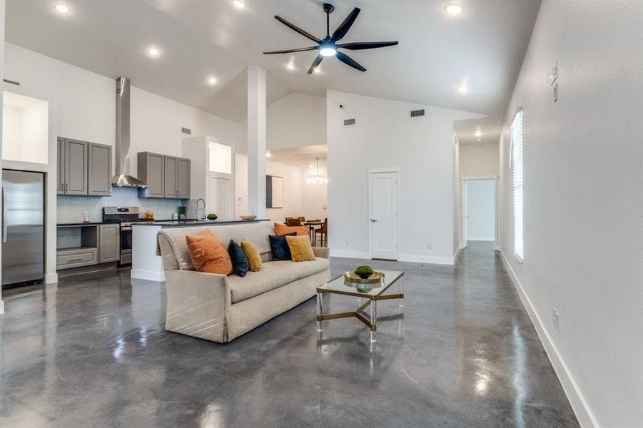 Living room featuring high vaulted ceiling, sink, and ceiling fan with notable chandelier