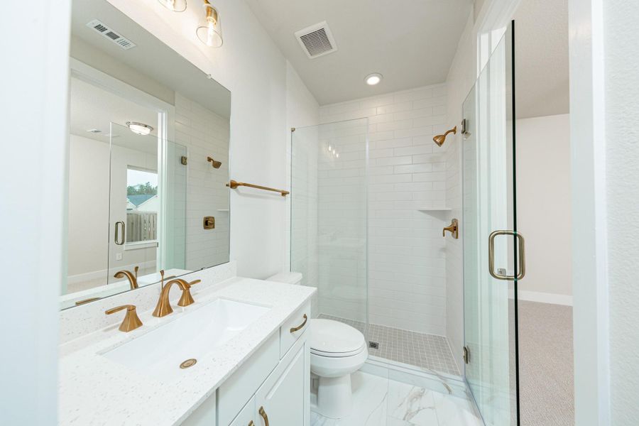 The private en suite bathroom features a modern white vanity with matte gold fixtures, mirror, lights, recessed lighting over the walk-in shower.