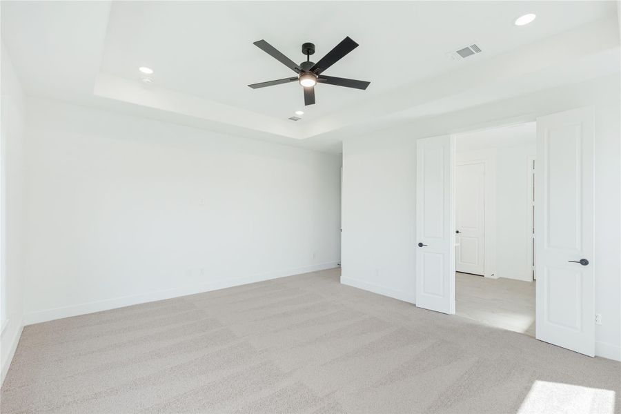 Empty bedroom with tray ceiling, black ceiling fan, carpet flooring, and white walls