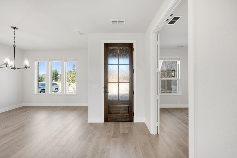 Open entryway with dark wood glass-panel front door, light hardwood floors, and chandelier Open entryway with dark wood glass-panel front door, light hardwood floors, and chandelier