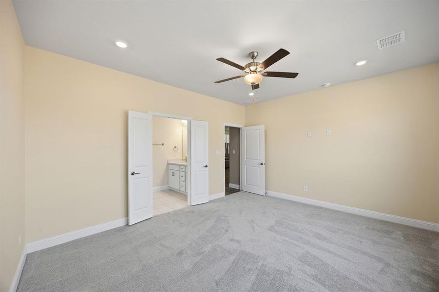 1st level primary bedroom with light colored carpet, recessed lighting, ceiling fan, and connected bathroom