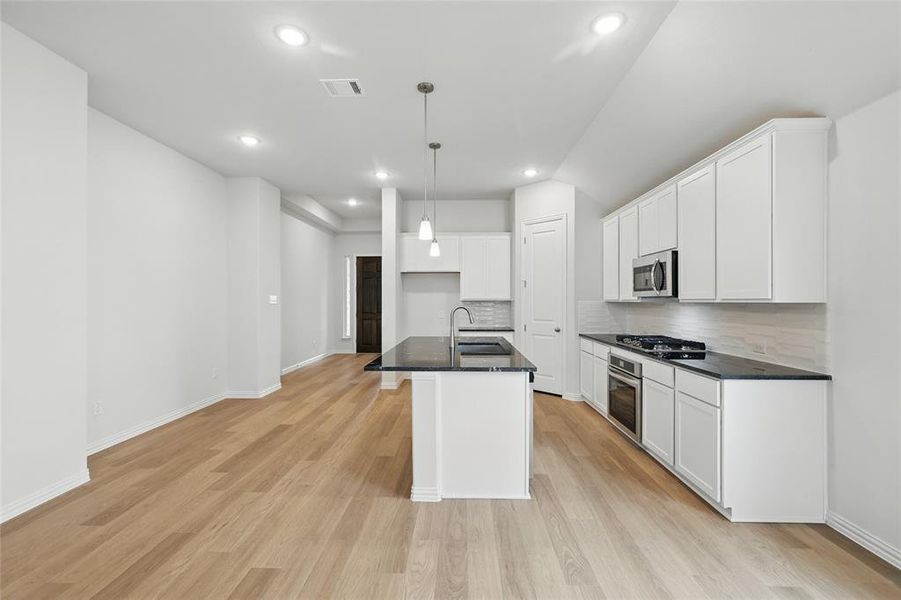 Kitchen with white cabinetry, decorative backsplash, an island with sink, and light wood finished floors