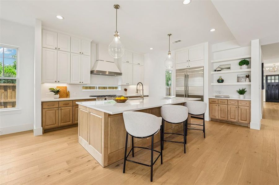 Gourmet kitchen featuring a large central island with seating, stainless steel appliances, a range hood, wood-finish flooring, and open shelving