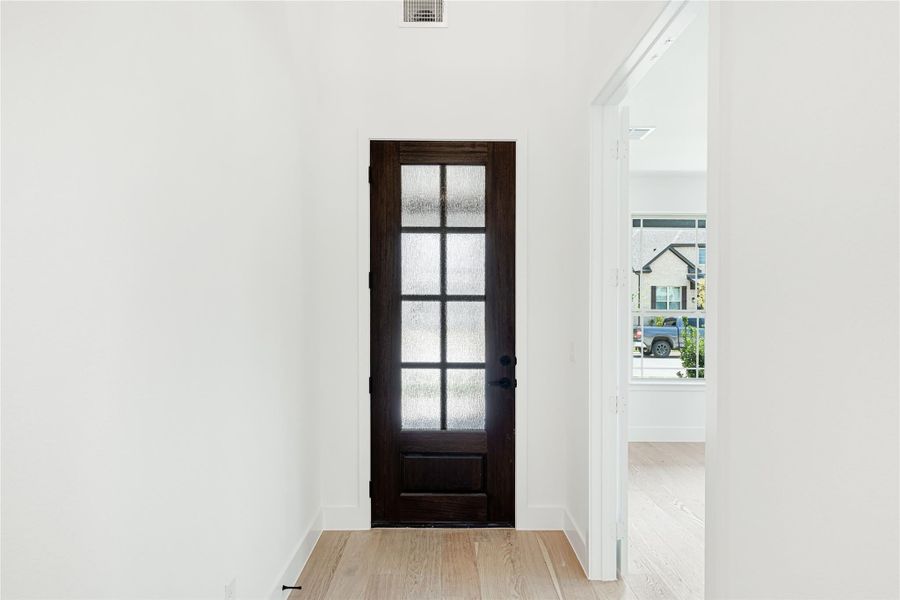 Entryway with dark wood French door featuring glass panels and light hardwood floors Entryway with dark wood French door featuring glass panels and light hardwood floors