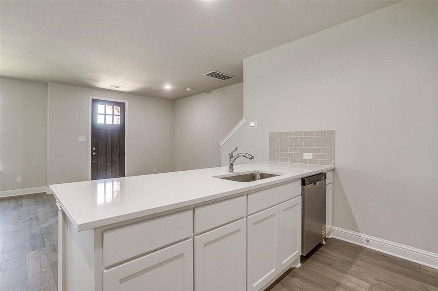 Kitchen with a peninsula, light wood-type flooring, white cabinets, light countertops, and dishwasher Kitchen with a peninsula, light wood-type flooring, white cabinets, light countertops, and dishwasher