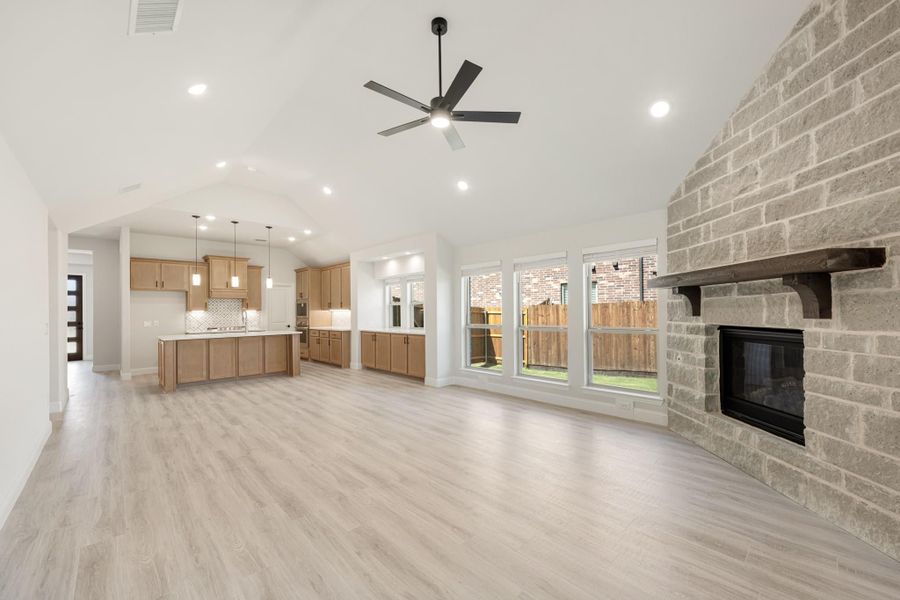 Open living area with brick fireplace, ceiling fan, and kitchen with island in background