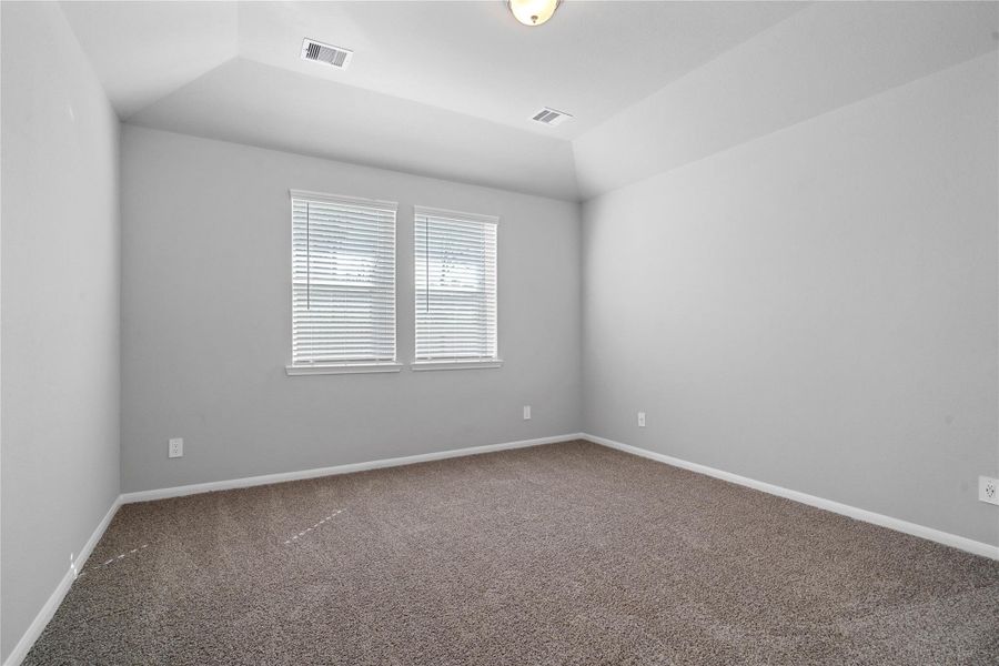 The primary bedroom provides a peaceful escape with a bright, neutral palette, sloped ceilings, large windows (fitted with blinds), and plush carpet flooring, creating a calm and restorative atmosphere to end your day.