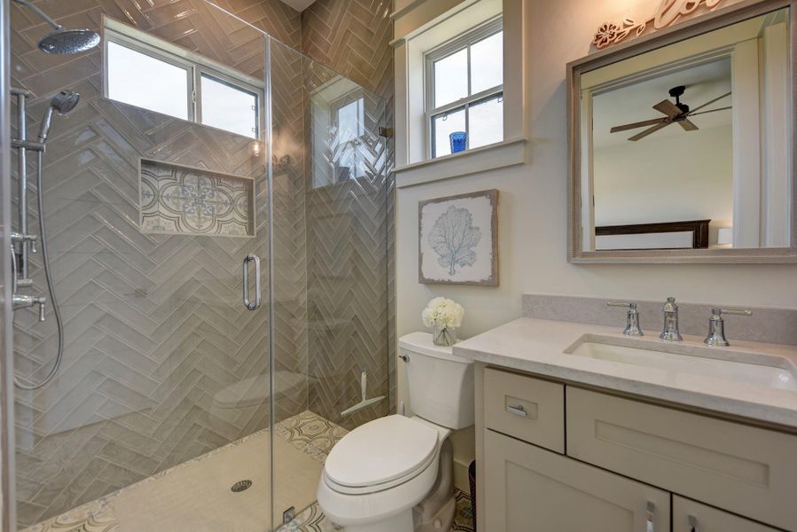Herringbone tiled shower with glass enclosure and a stylish vanity create a modern bath.