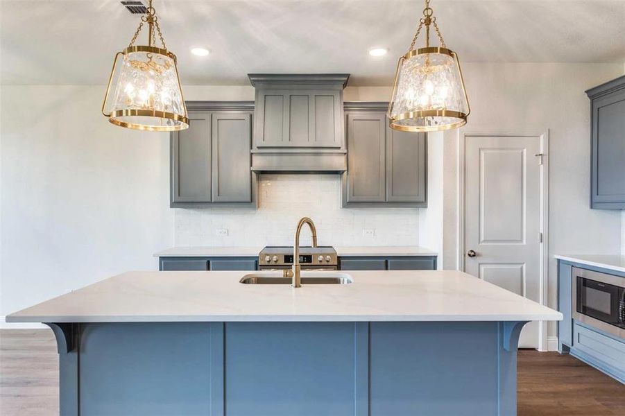 Kitchen with dark wood-style flooring, gray cabinets, light countertops, backsplash, and hanging light fixtures Kitchen with dark wood-style flooring, gray cabinets, light countertops, backsplash, and hanging light fixtures