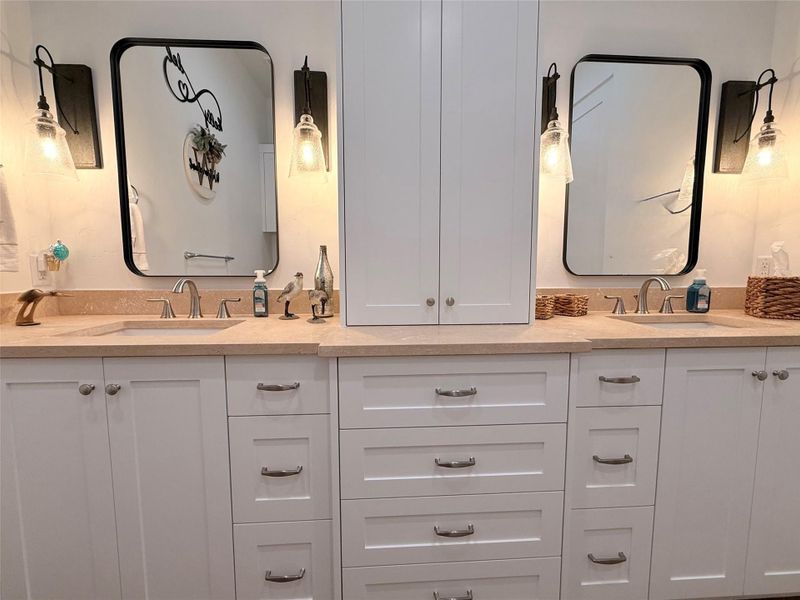This bathroom features a dual-sink vanity with elegant white cabinetry and modern fixtures. It has ample storage space with multiple drawers and cabinets, complemented by stylish mirrors and soft lighting.