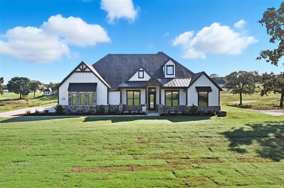 Modern farmhouse style home featuring a front yard, a standing seam roof, a metal roof, board and batten siding, and stone siding Modern farmhouse style home featuring a front yard, a standing seam roof, a metal roof, board and batten siding, and stone siding