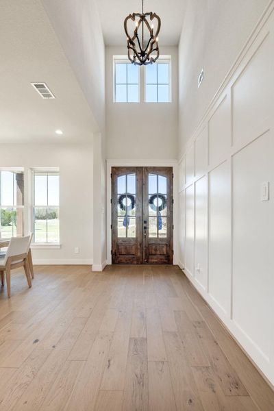 Foyer entrance featuring light wood-type flooring, hanging lights, french doors, healthy amount of natural light, and a high ceiling