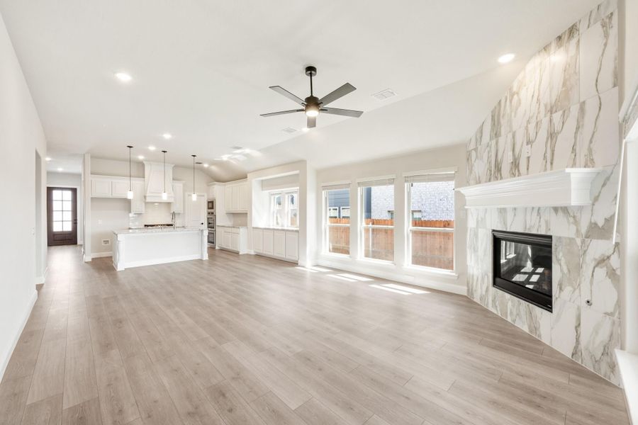 Open-concept living area with marble fireplace, hardwood floors, and kitchen with white cabinets in background Open-concept living area with marble fireplace, hardwood floors, and kitchen with white cabinets in background