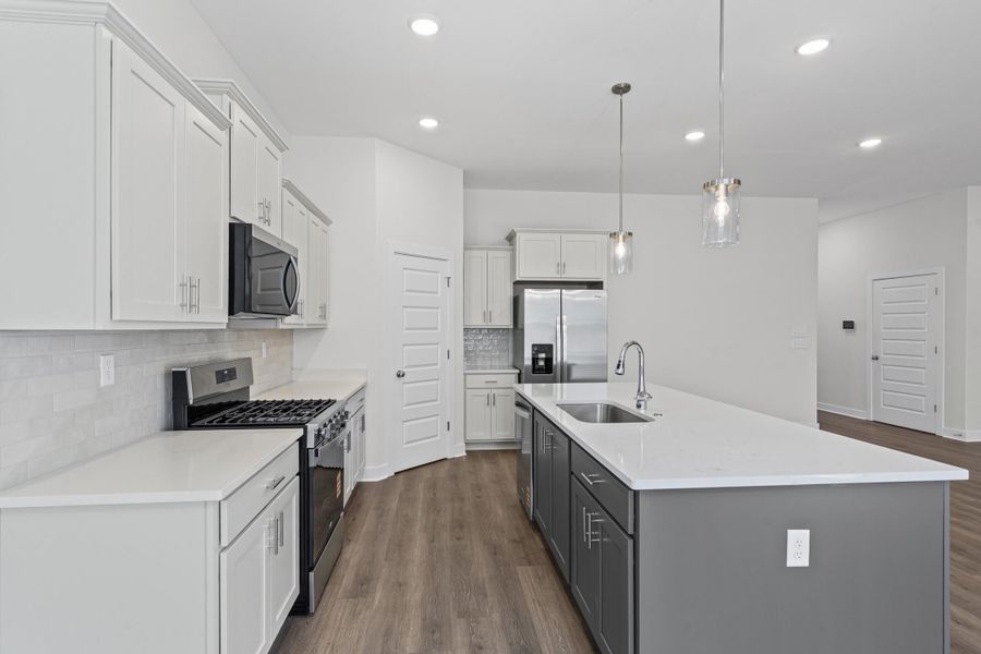 Dual tone kitchen featuring stainless steel appliances, dual tone cabinetry, dark wood-style floors, hanging light fixtures, and a kitchen island with sink