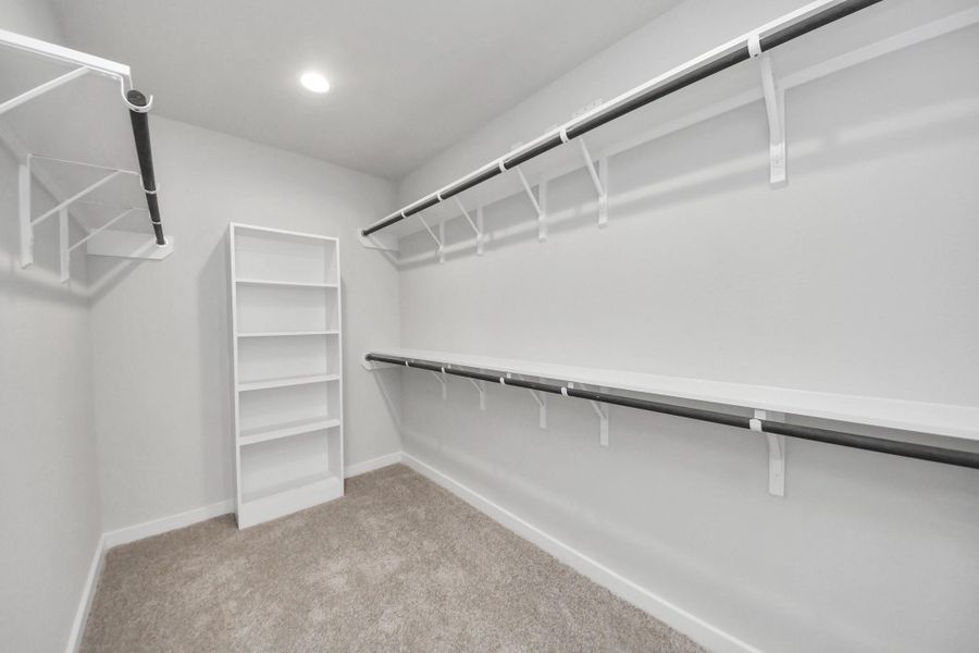 Walk-in closet that epitomizes luxury and practicality. This generously sized space features built-in shelving, offering abundant room for impeccable organization. High ceilings and recessed lighting create a bright and welcoming ambiance. Sample photo of completed home with similar floor plan. Actual colors and selections may vary.