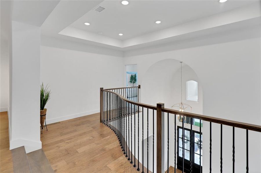Second-level landing featuring wood-finish flooring, a wrought iron and wood baluster railing, recessed lighting, and a tray ceiling