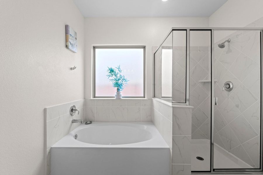 Bright bathroom featuring a built-in tub, separate glass-enclosed shower, frosted window, chrome fixtures, and white tile surrounds