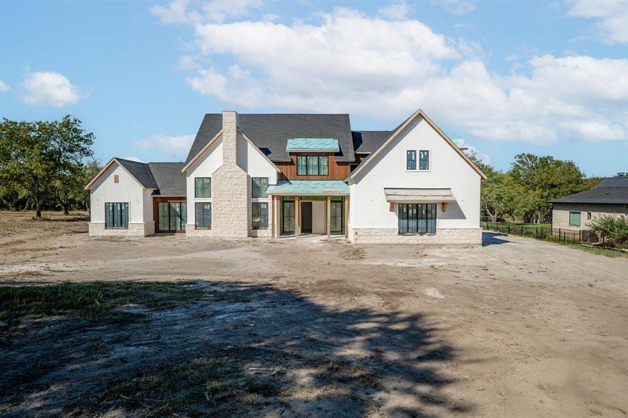 Front view of property with stone siding, a chimney, a patio, and a shingled roof Front view of property with stone siding, a chimney, a patio, and a shingled roof