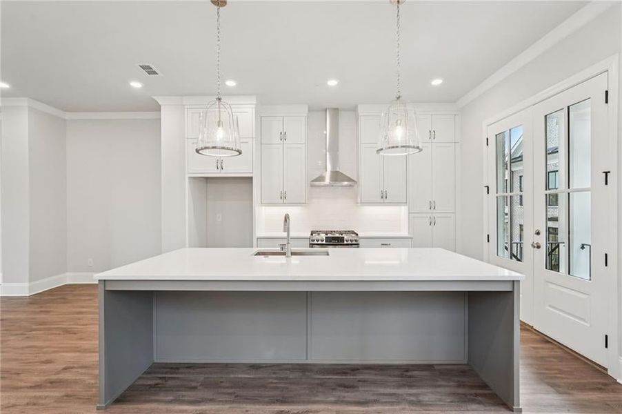 Kitchen with dark wood-style floors, white cabinets, crown molding, hanging light fixtures, and stainless steel range with gas stovetop