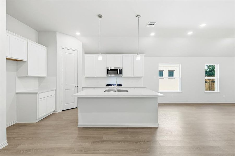 Kitchen with a center island with sink, white cabinets, hanging light fixtures, stainless steel microwave, and light wood-style flooring