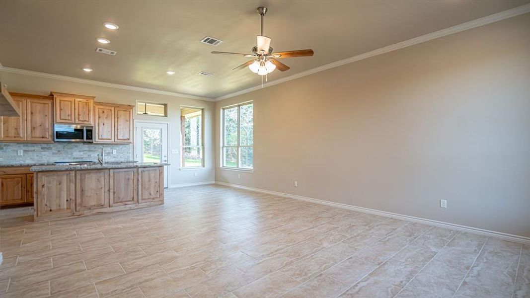 Kitchen with an island with sink, recessed lighting, crown molding, stainless steel microwave, and light stone counters