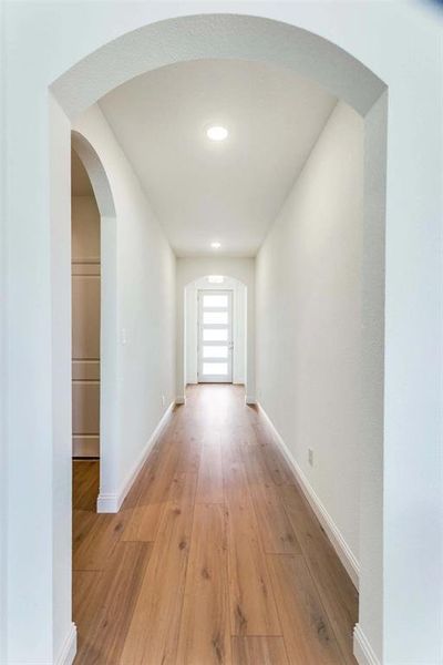 Hall featuring arched walkways, light wood-style flooring, and baseboards