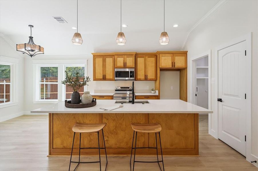 Kitchen featuring brown cabinets, a kitchen bar, light wood finished floors, ornamental molding, and appliances with stainless steel finishes