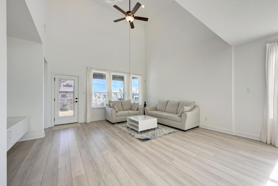 Living area featuring light wood-style flooring, a ceiling fan, and high vaulted ceiling
