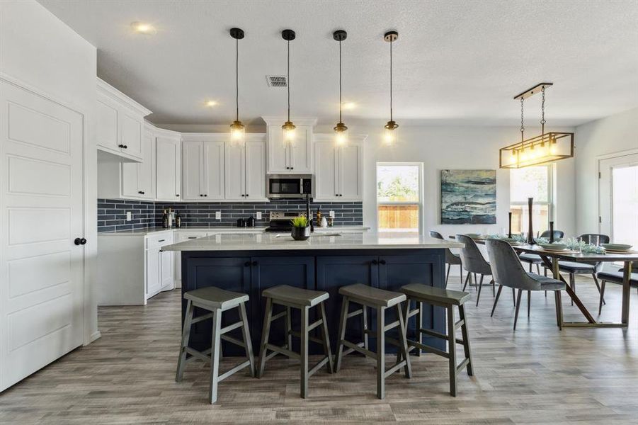 Kitchen with light hardwood / wood-style flooring, stainless steel appliances, pendant lighting, a kitchen breakfast bar, and a center island with sink