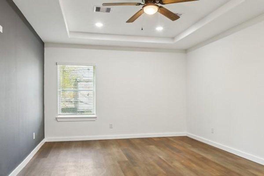 Step into the inviting primary bedroom, featuring a modern ceiling fan, elegant tray ceiling, and abundant natural light. Step into the inviting primary bedroom, featuring a modern ceiling fan, elegant tray ceiling, and abundant natural light.