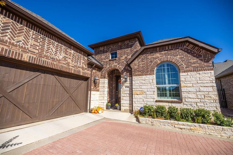 French provincial home featuring brick siding, an attached garage, and decorative driveway French provincial home featuring brick siding, an attached garage, and decorative driveway