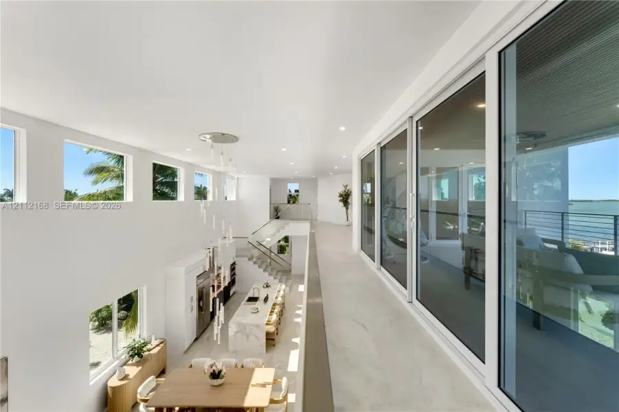 Open-concept upper level featuring large-format tile flooring, a multi-story glass pendant chandelier, expansive floor-to-ceiling sliding glass doors, and a metal-railing staircase Open-concept upper level featuring large-format tile flooring, a multi-story glass pendant chandelier, expansive floor-to-ceiling sliding glass doors, and a metal-railing staircase