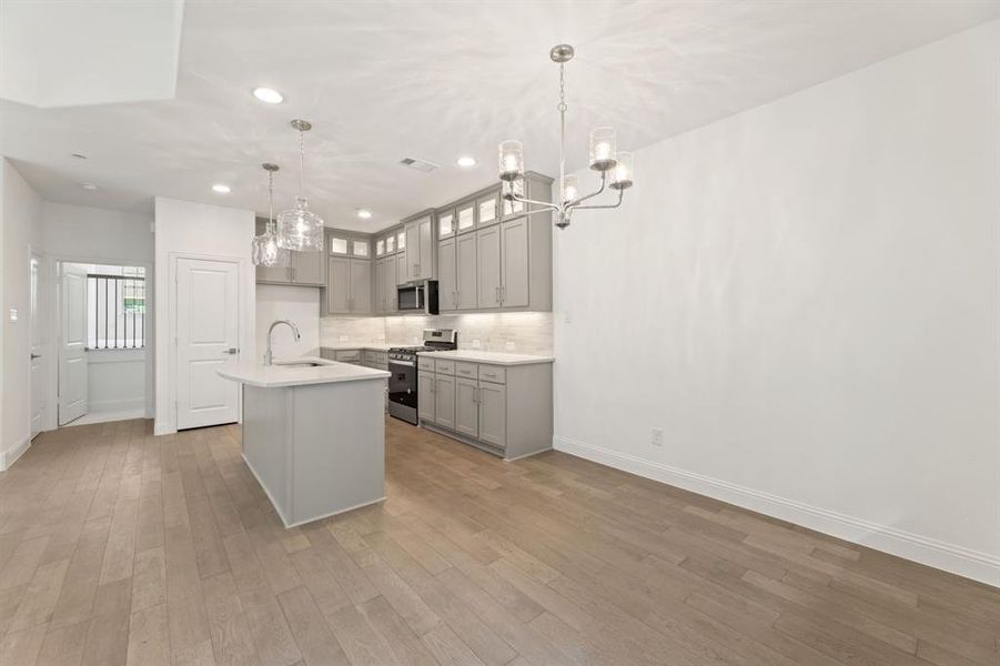 Kitchen featuring hanging light fixtures, a center island with sink, appliances with stainless steel finishes, light wood-type flooring, and sink