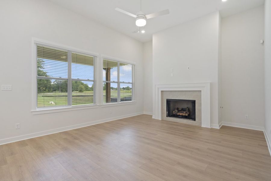Spacious room featuring vaulted ceilings, wood-finish flooring, a contemporary fireplace with a white mantel, recessed lighting, and multiple windows