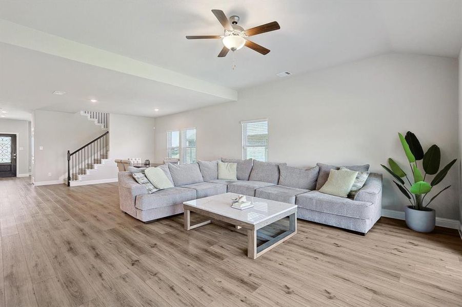 Living room with ceiling fan, light wood-type flooring, and lofted ceiling