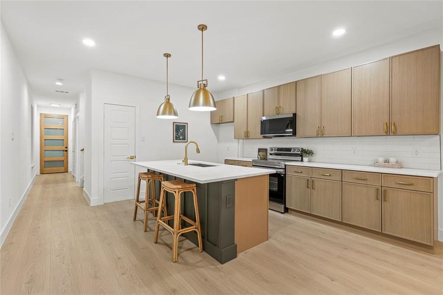 Kitchen with appliances with stainless steel finishes, tasteful backsplash, a kitchen bar, a kitchen island with sink, and pendant lighting