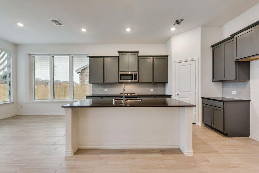 Kitchen with an island with sink, gray cabinets, decorative backsplash, and sink