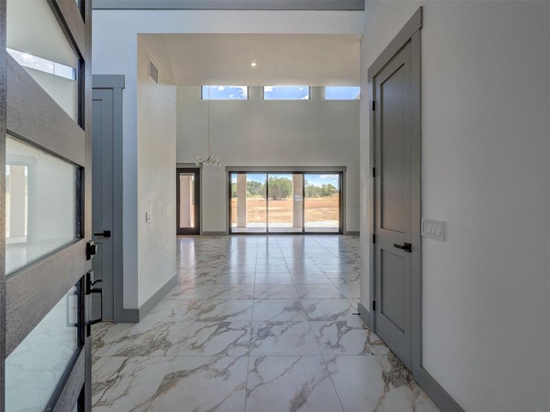 Polished tile flooring guides the eye through a soaring entry toward distant outdoor views.