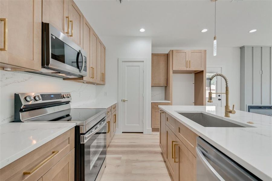 Kitchen with sink, decorative light fixtures, appliances with stainless steel finishes, light hardwood / wood-style floors, and light brown cabinets