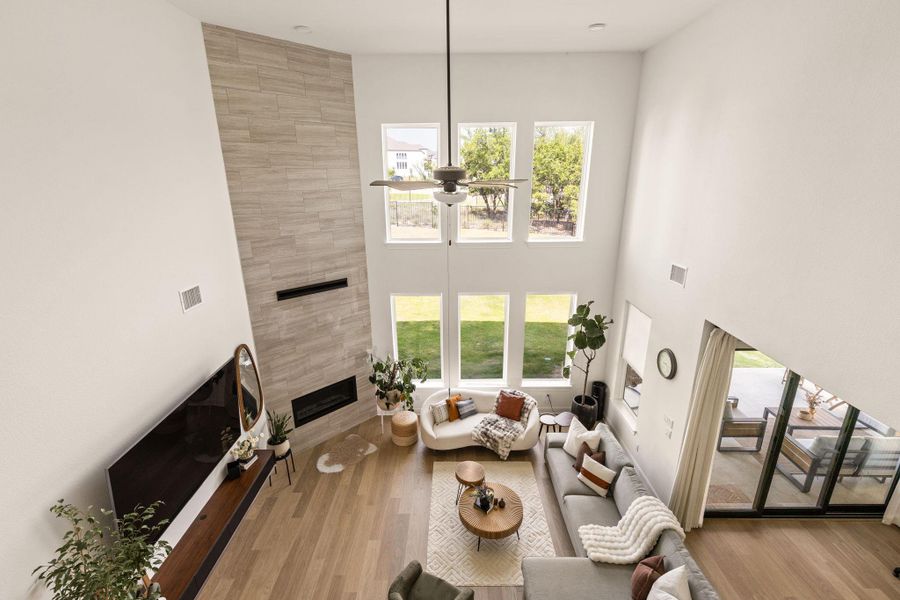 Great room featuring a vaulted ceiling with a ceiling fan, a tiled accent wall with an inset linear fireplace, multiple large windows, and light wood-finish flooring