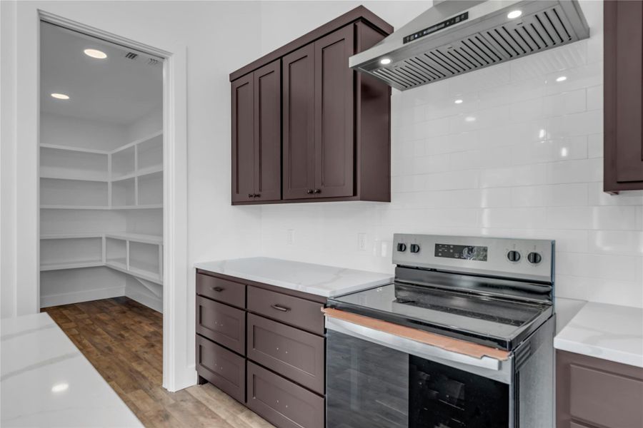 Dark cabinetry and light countertops complement a functional kitchen layout with a nearby walk-in pantry.