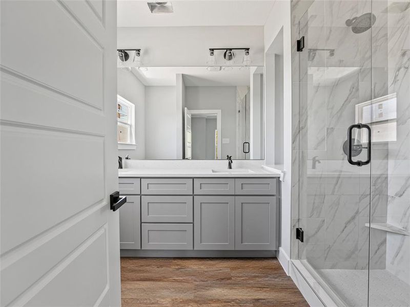 Full bath featuring a marble finish shower, wood finished floors, and double vanity